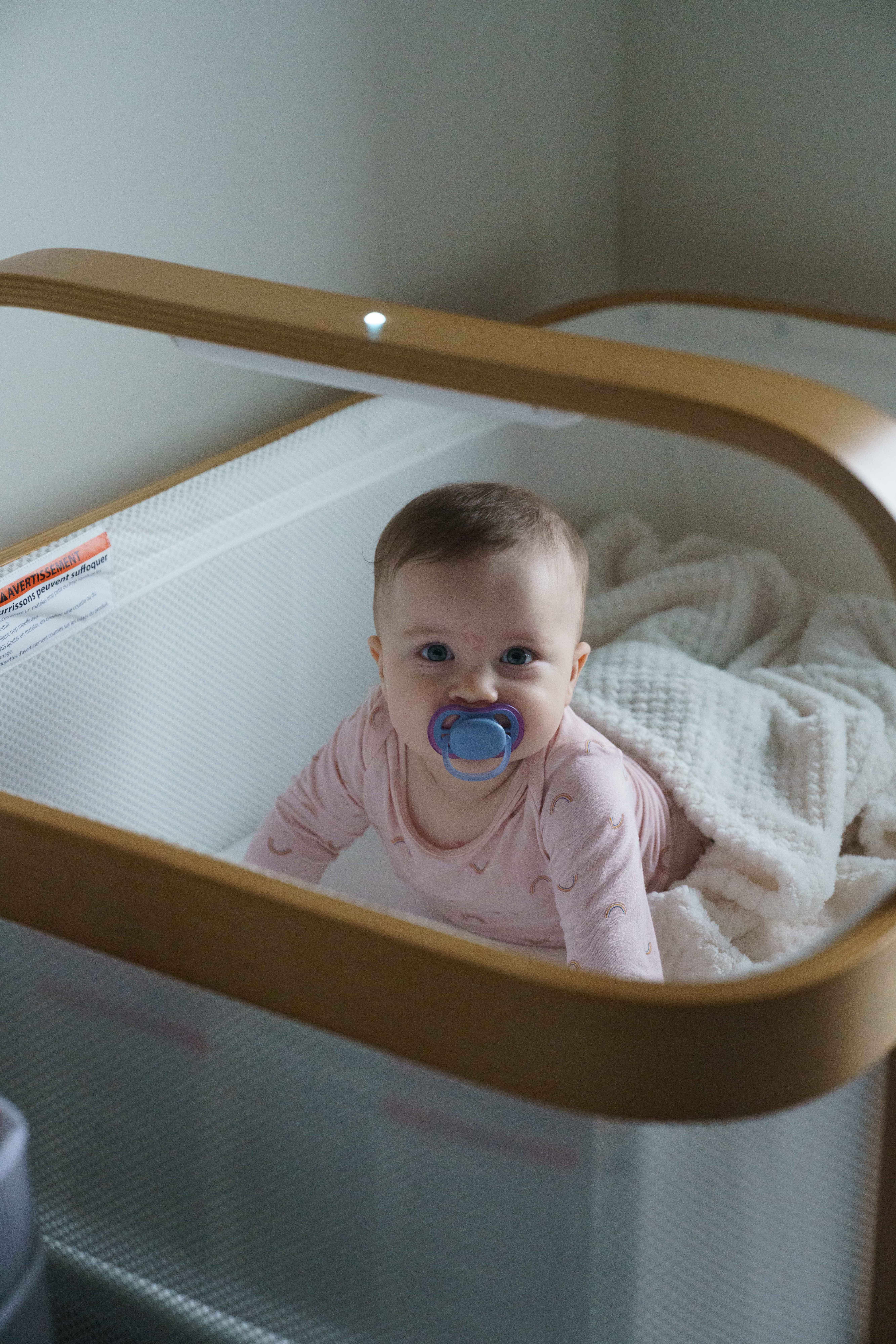 Isabella in pink outfit with pacifier in wooden bassinet